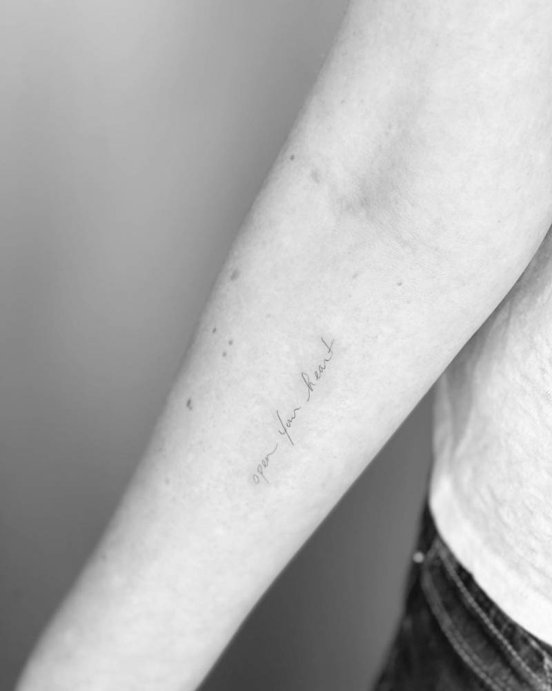 "Open your heart" lettering tattoo on the inner forearm.