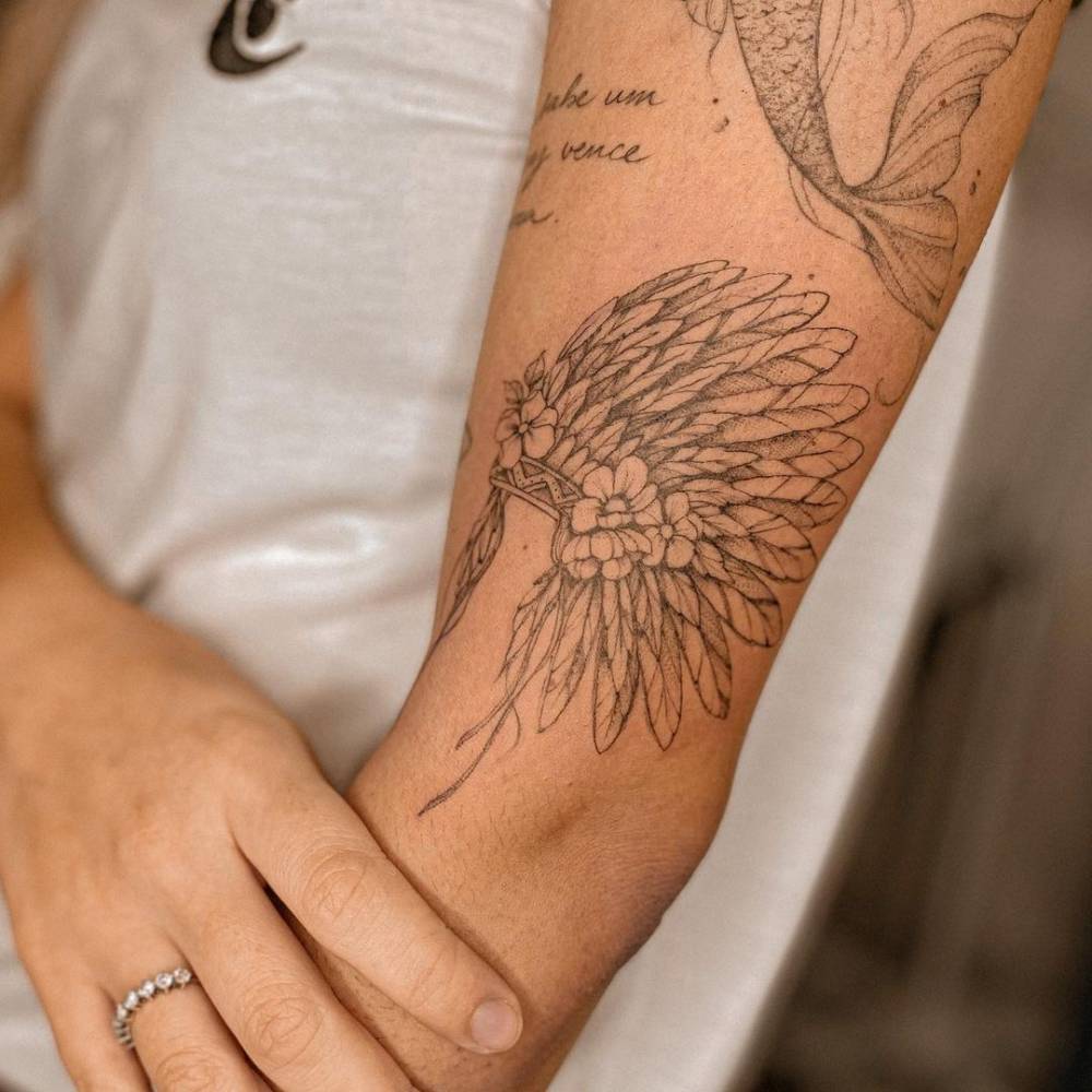 Fine line war bonnet tattoo on the upper arm.