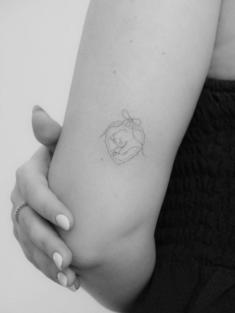 Cat pendant tattoo in fine line style located on the tricep.