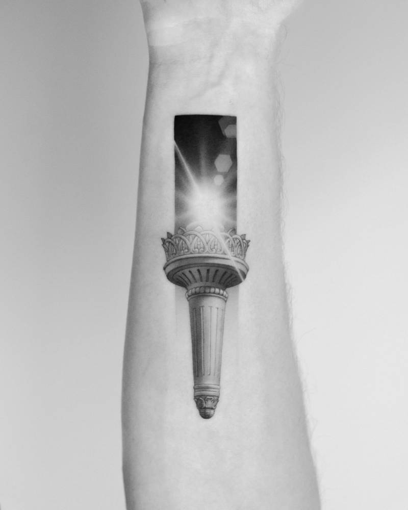 Statue of Liberty torch tattoo located on the inner forearm.