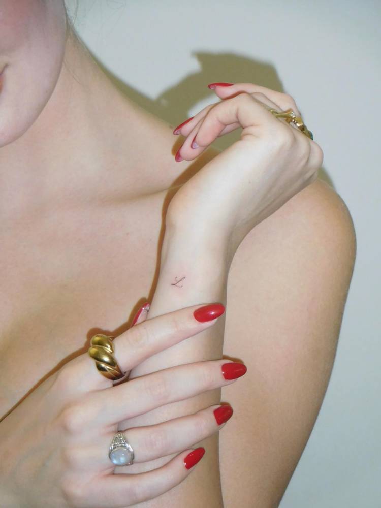 Tiny letter "L" tattoo in handwritten font located on the wrist.