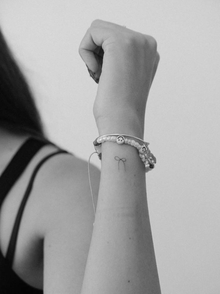 Tiny minimalistic bow tattoo located on the wrist.