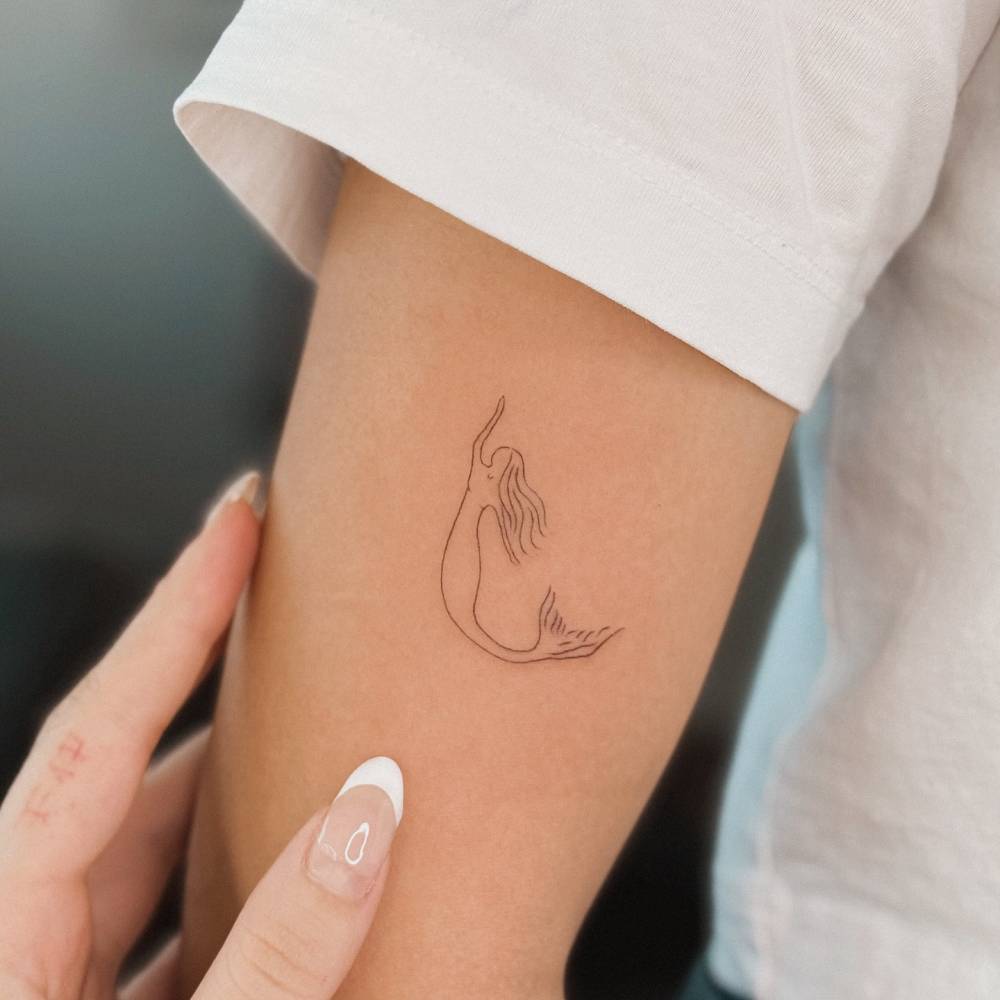 Minimalistic mermaid tattoo in fine line style placed on the upper arm.