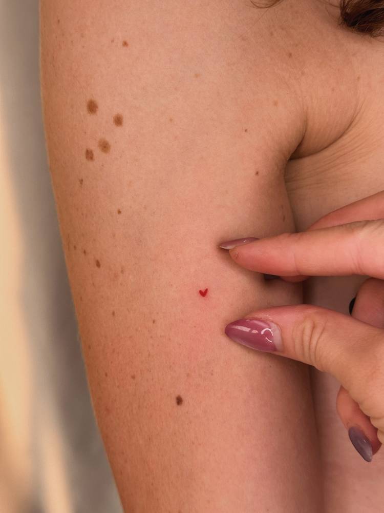 Tiny red heart tattoo in minimalistic style located on the upper arm.