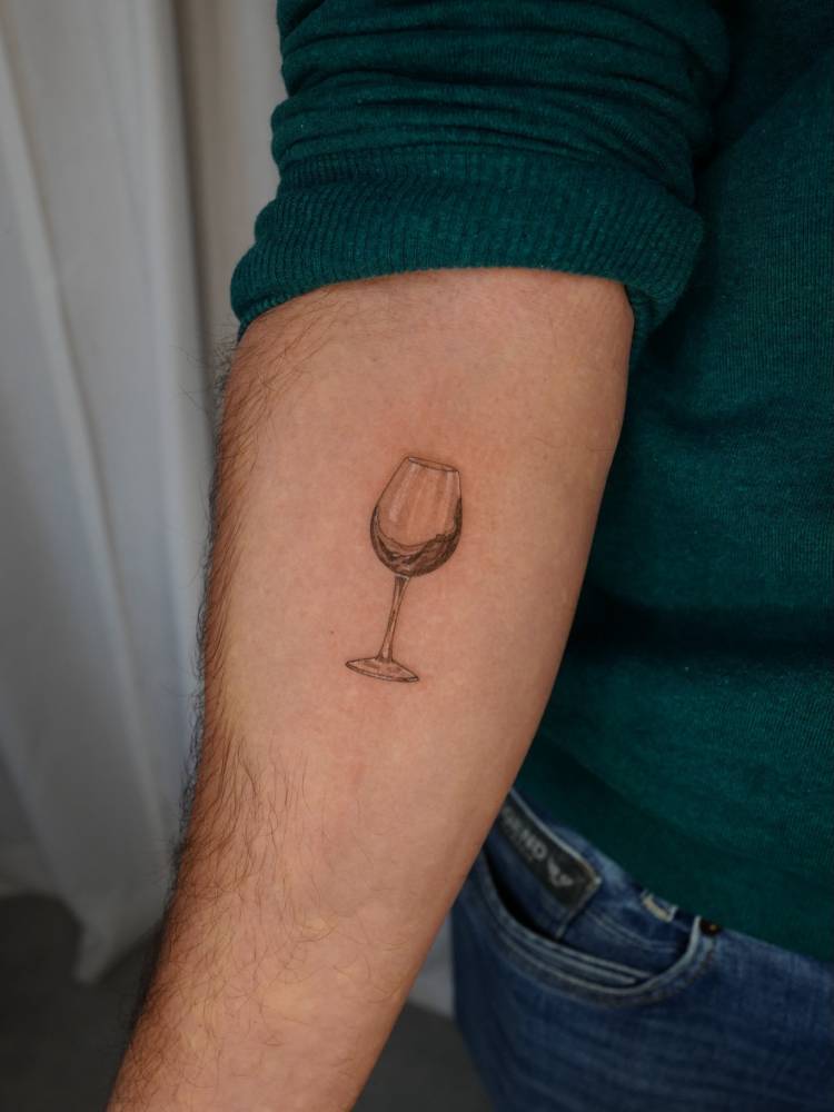 Wine glass tattoo in illustrative style placed on the inner forearm.