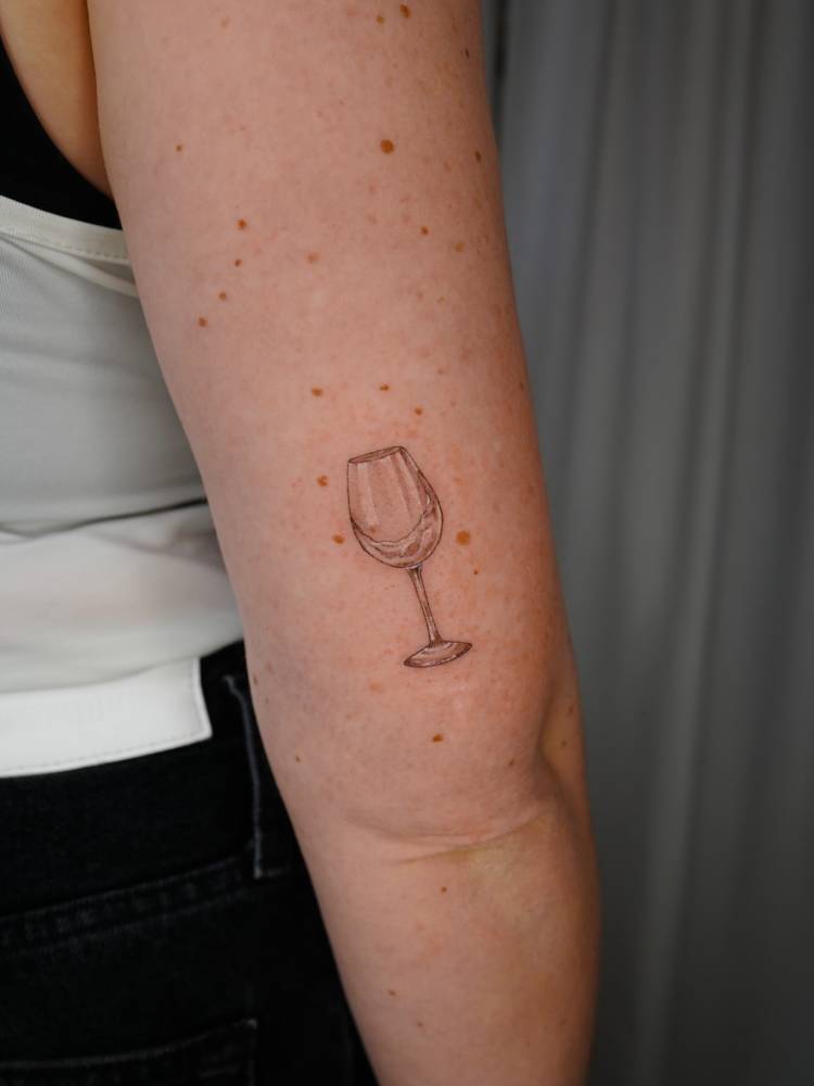 Wine glass tattoo in illustrative style placed on the tricep.