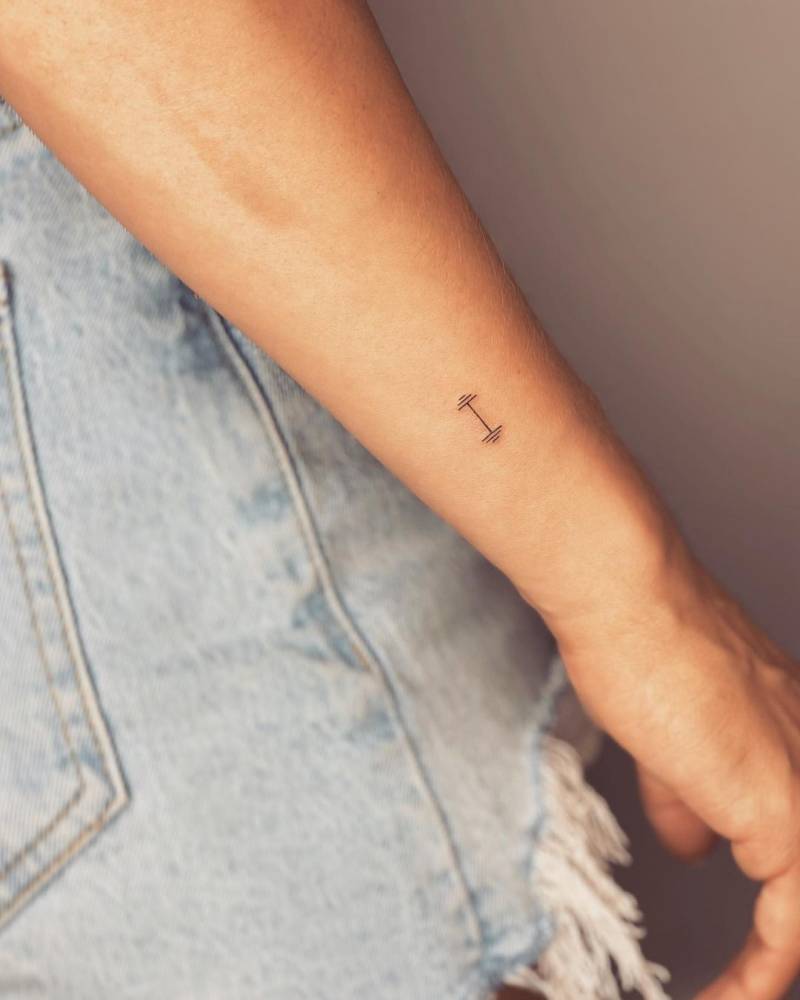 Tiny minimalistic dumbbell tattoo located on the wrist.