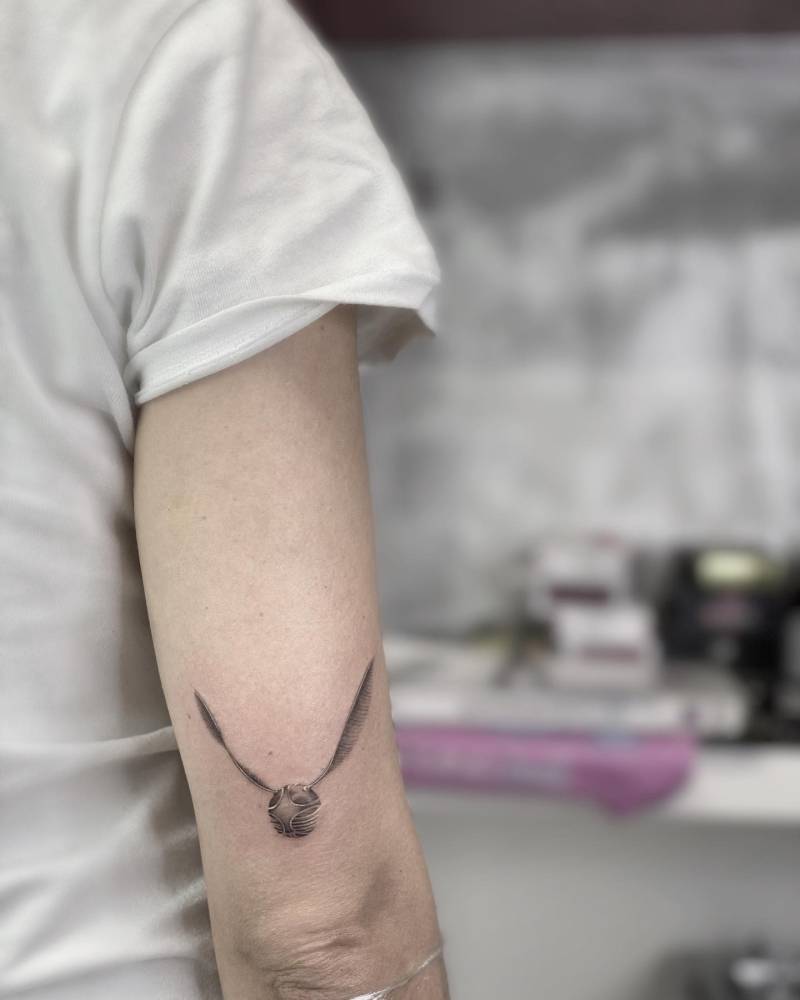 Golden snitch tattoo in micro-realistic style located on the tricep.
