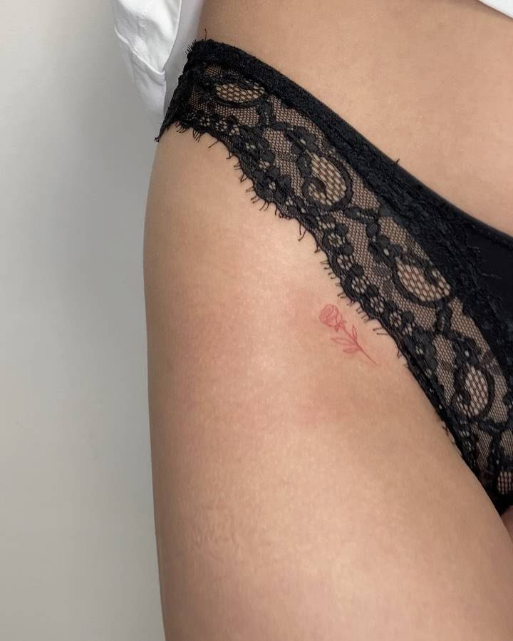 Fine line style red rose tattoo placed on the pelvis.