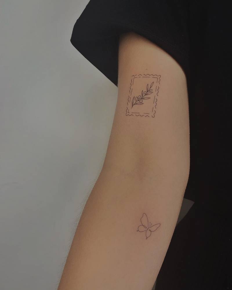 Fine line style olive branch stamp and butterfly tattoos located on the arm.