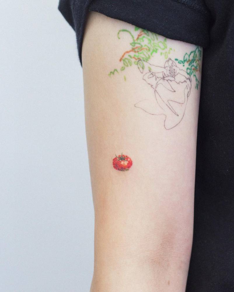 Watercolor style little tomato tattoo located on the upper arm.