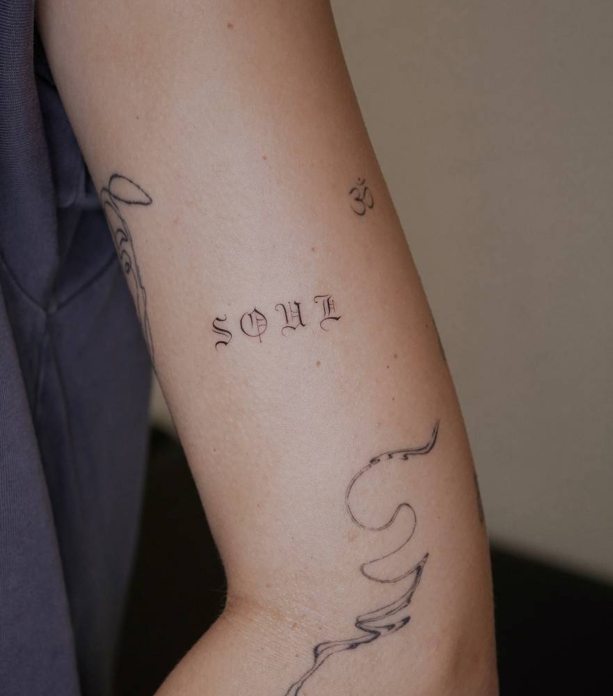 Lettering tattoo of the word "soul" in gothic font located on the upper arm.