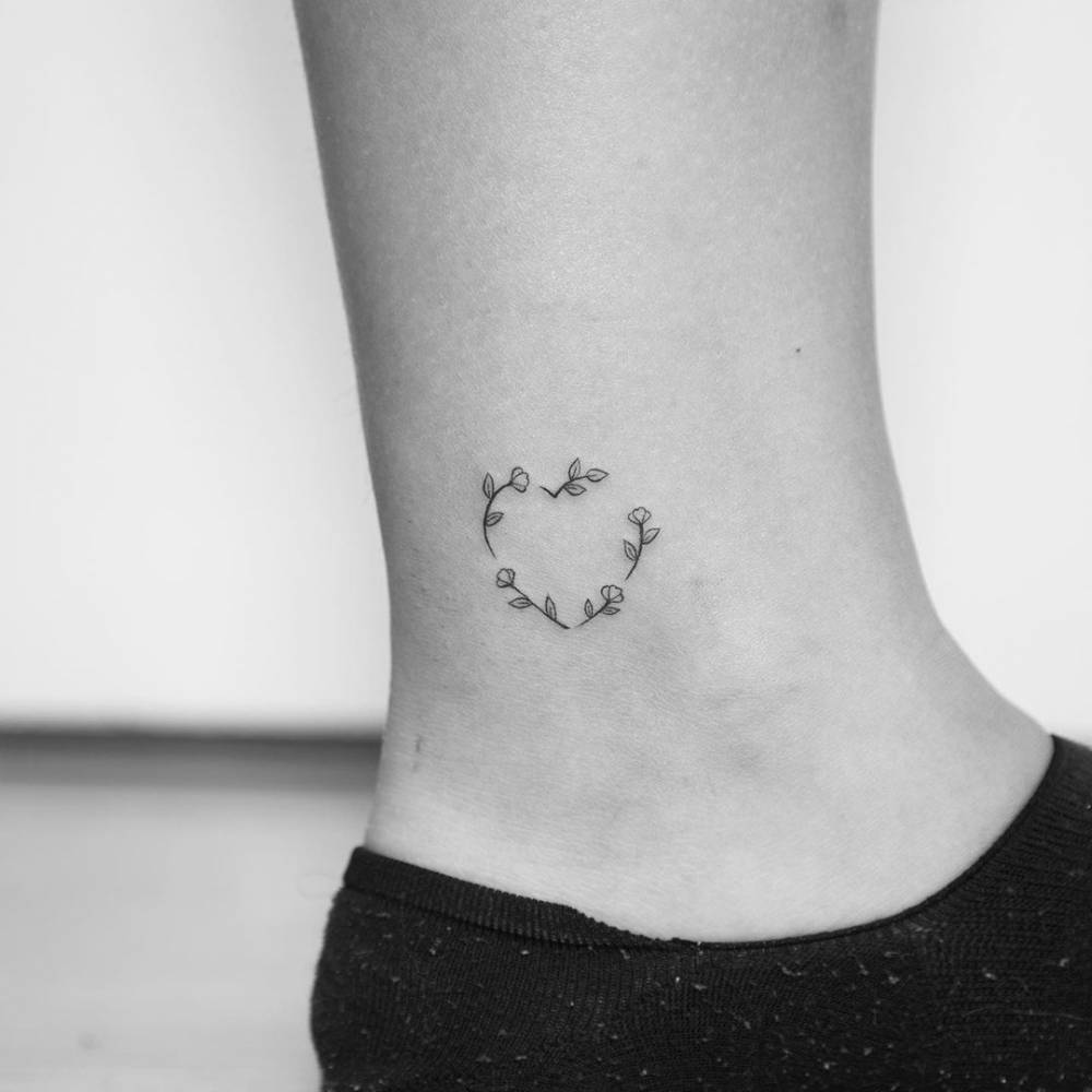 Fine line heart shaped flower wreath tattoo on the ankle.