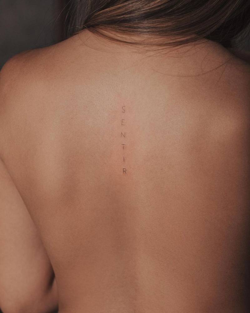 "Sentir" lettering tattoo on the upper back.