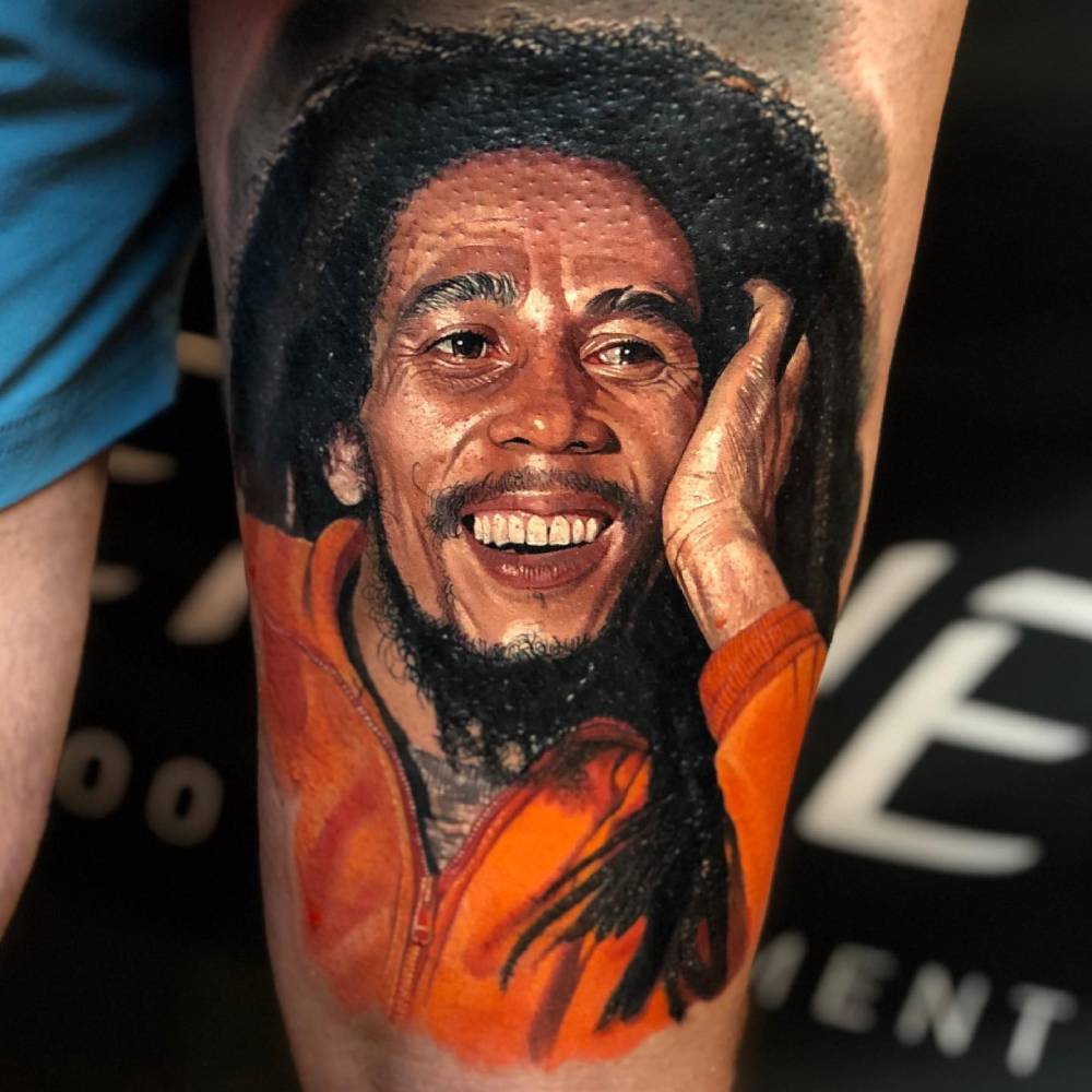 Bob Marley portrait tattoo located on the thigh, realistic style.