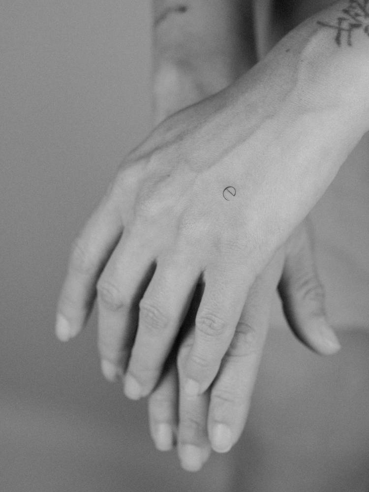 Tiny minimalistic letter "e" tattoo placed on the hand.