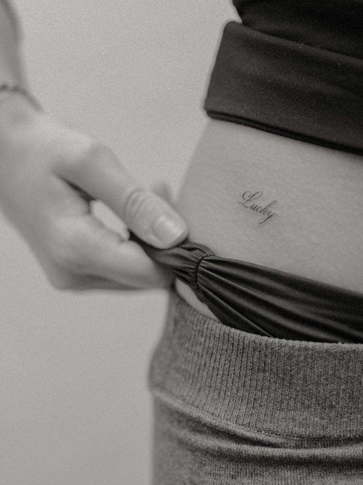 Serif font word "lucky" tattoo located on the hip.