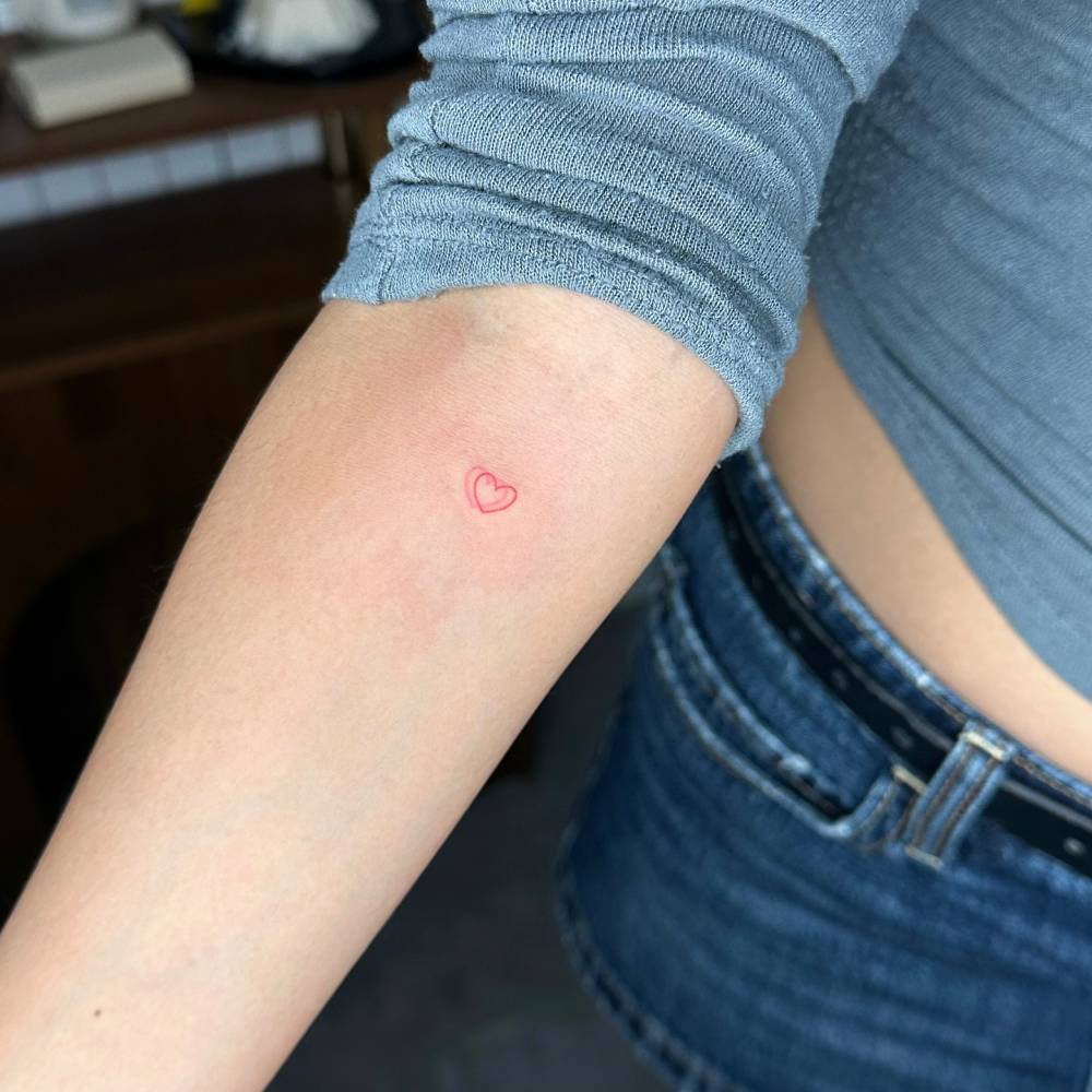 Hand poked minimalistic red heart tattoo located on the inner forearm.