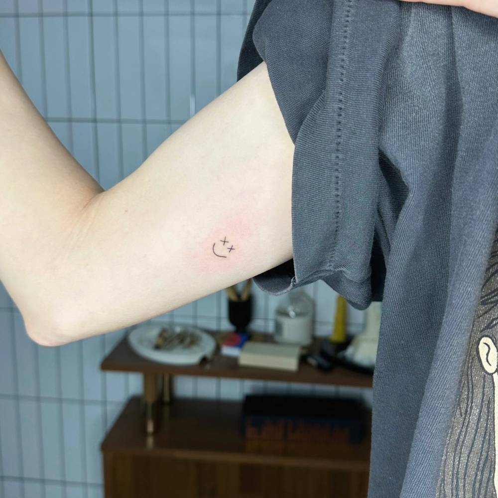 Hand poked smiley face in minimalistic style tattooed on the inner arm.