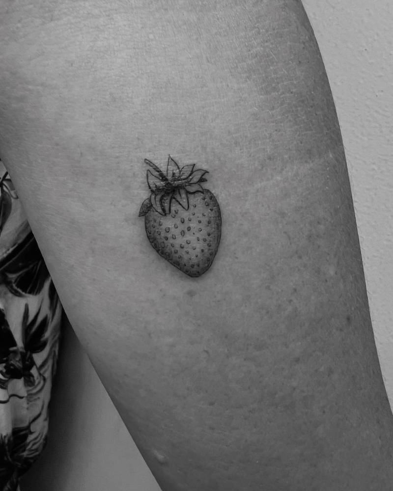 Little strawberry tattooed on the inner forearm, done in illustrative style.