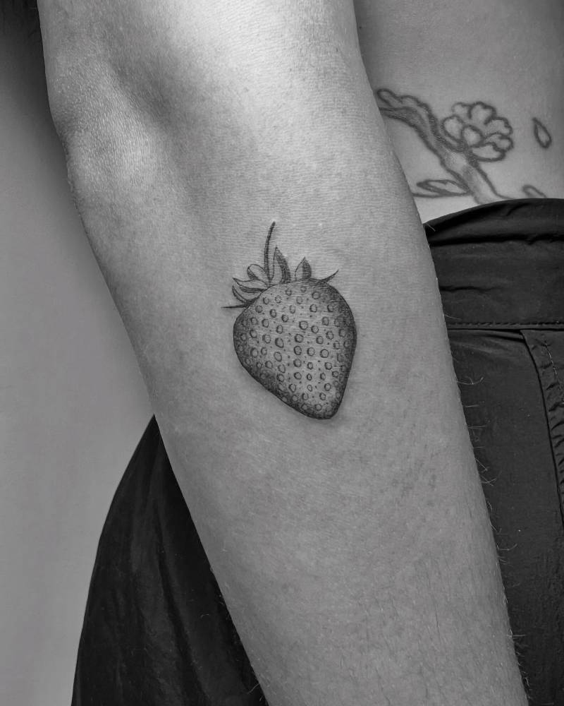Strawberry in illustrative style tattooed on the forearm.