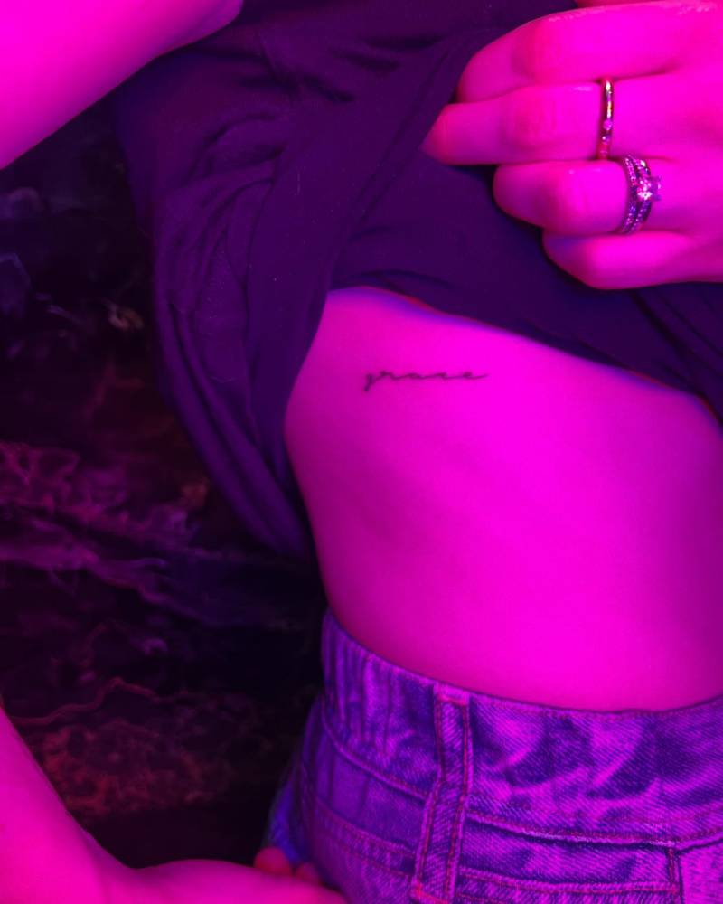 Handwritten lettering tattoo that says "grace" located on the rib.