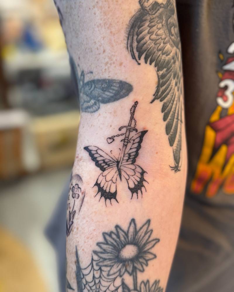 Butterfly and dagger tattoo in illustrative style placed on the inner forearm.