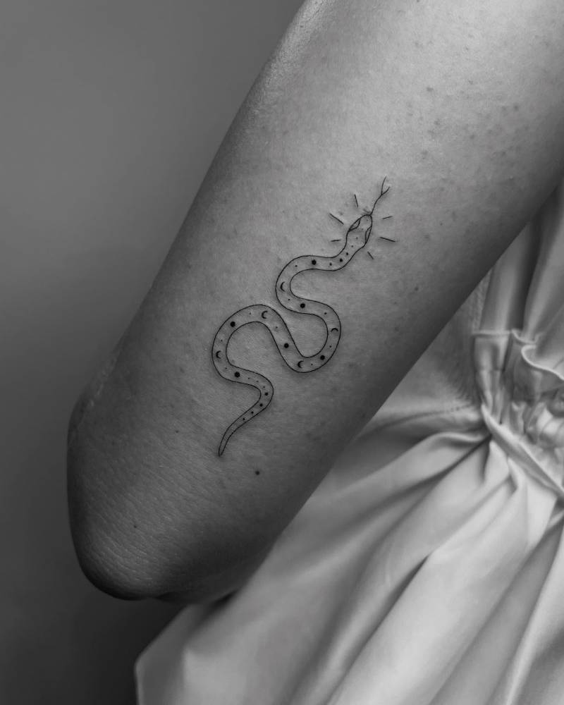 Snake tattoo in fine line style placed on the tricep.