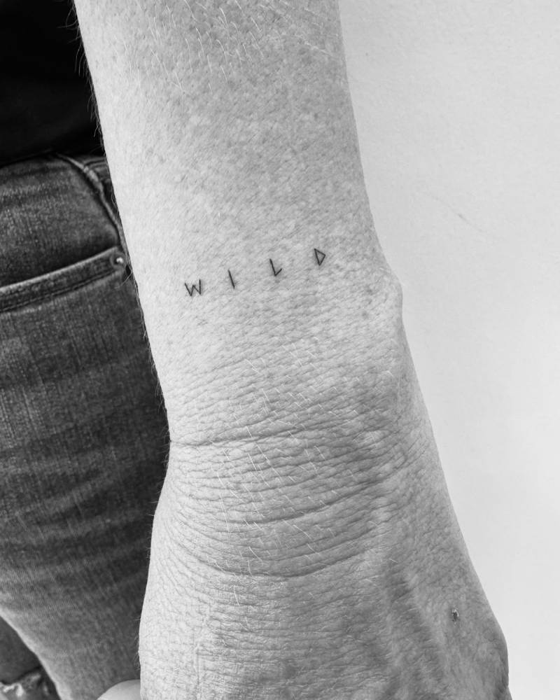 Handwritten font word "wild" tattooed on the wrist.