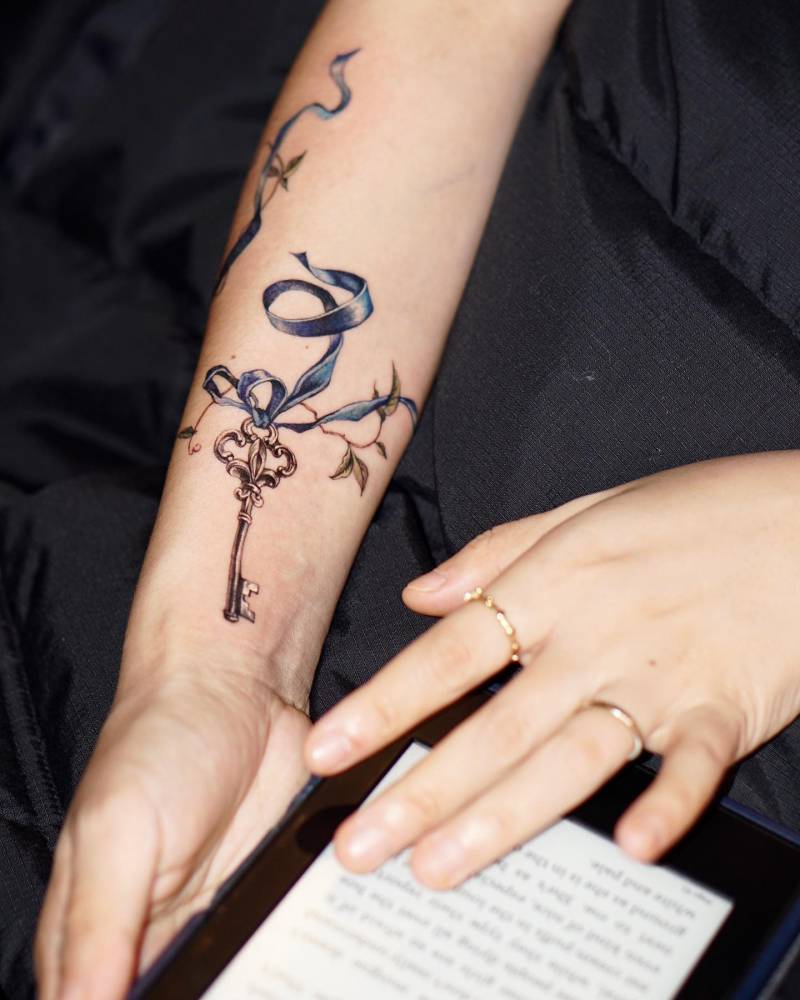 Watercolor style key tattoo located on the inner forearm.