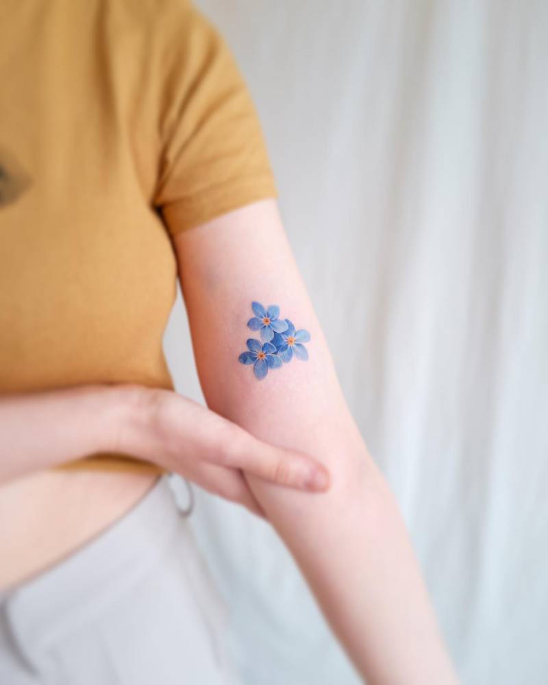 Watercolor style forget-me-not flowers tattoo located on the inner arm.