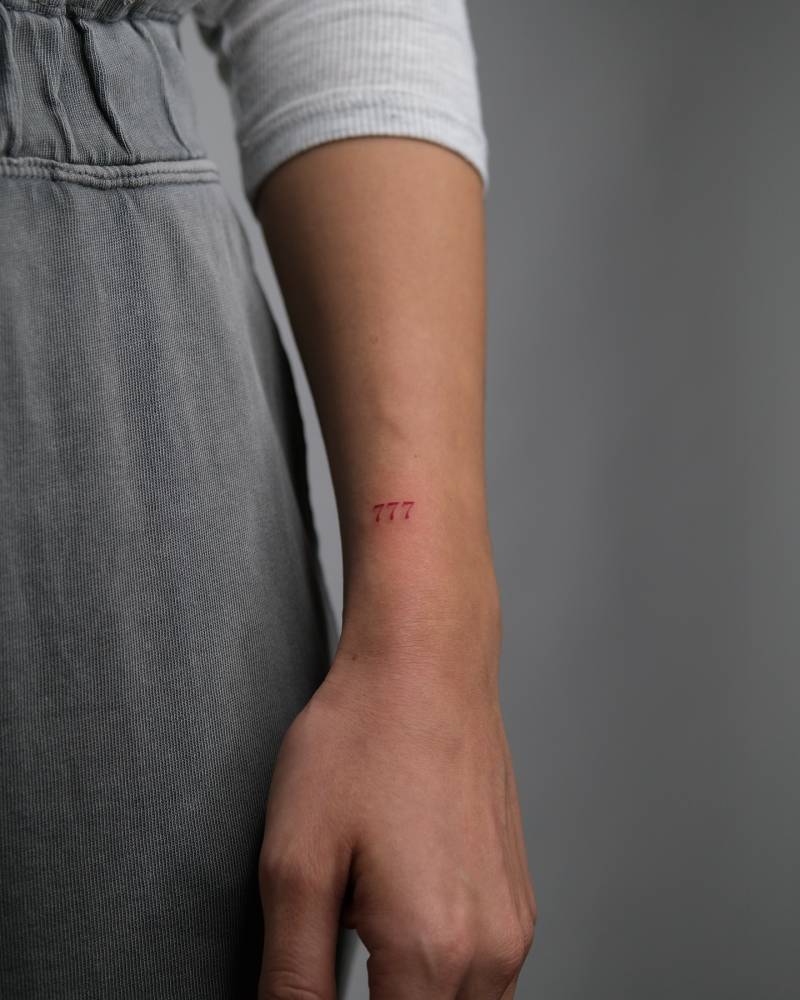 Number "777" tattoo in red ink located on the wrist.