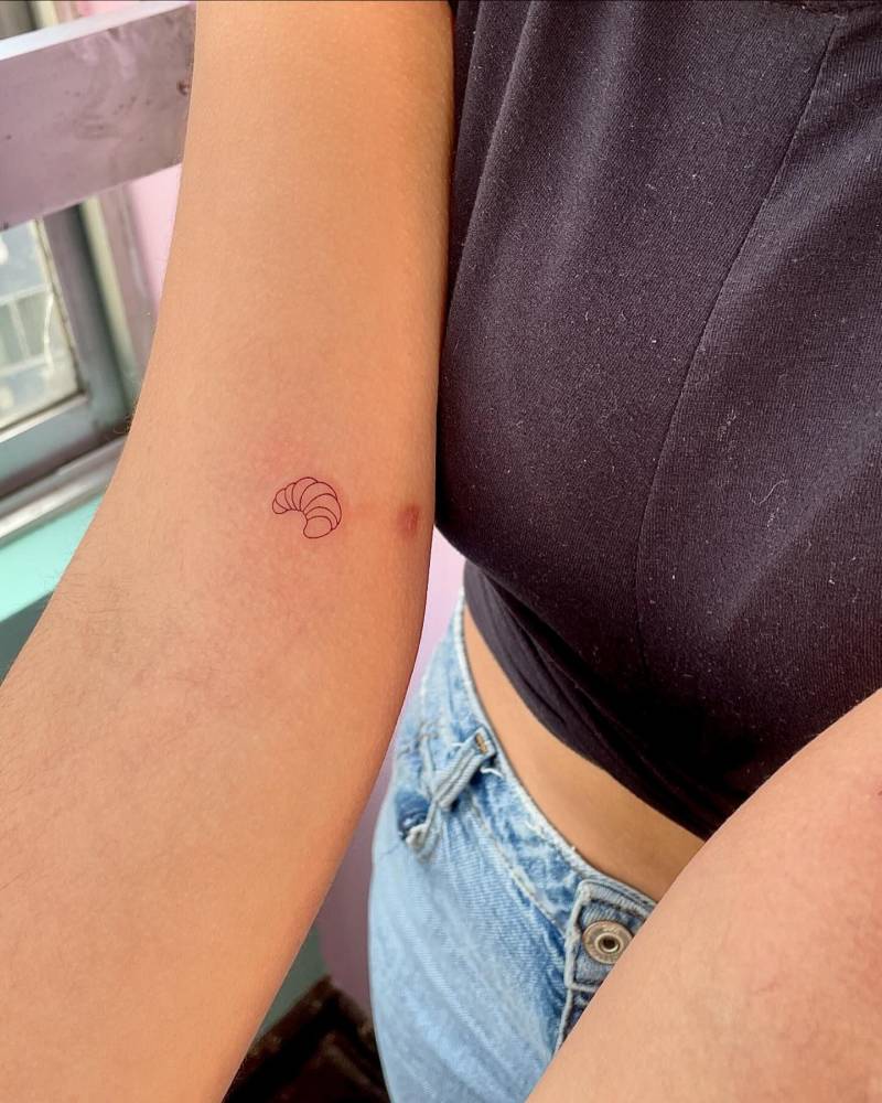 Fine line style minimalistic croissant tattoo located on the inner arm.
