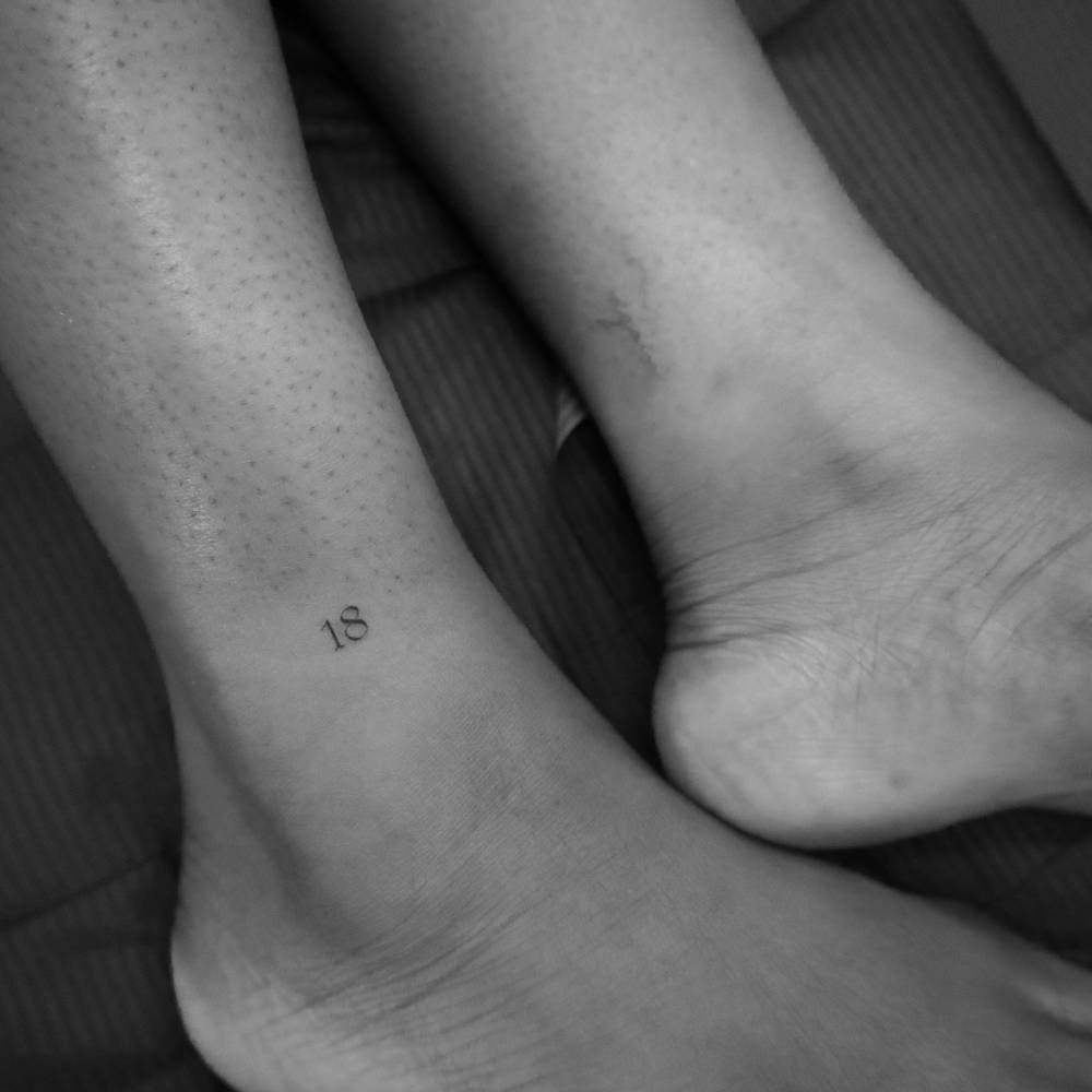 Number "18" tattooed on the ankle, minimalistic style.
