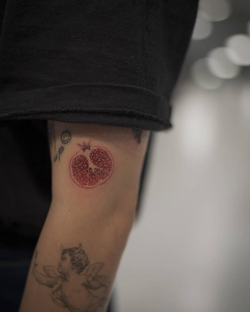 Micro-realistic style pomegranate tattoo located on the upper arm.