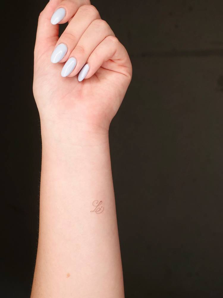 Letter "L" in script font tattooed on the wrist.