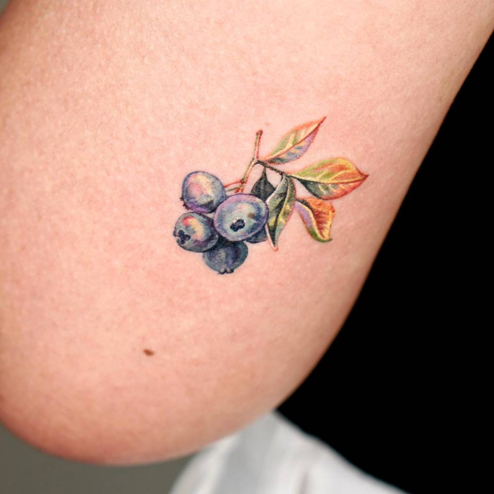 Watercolor style blueberries tattoo located on the tricep.