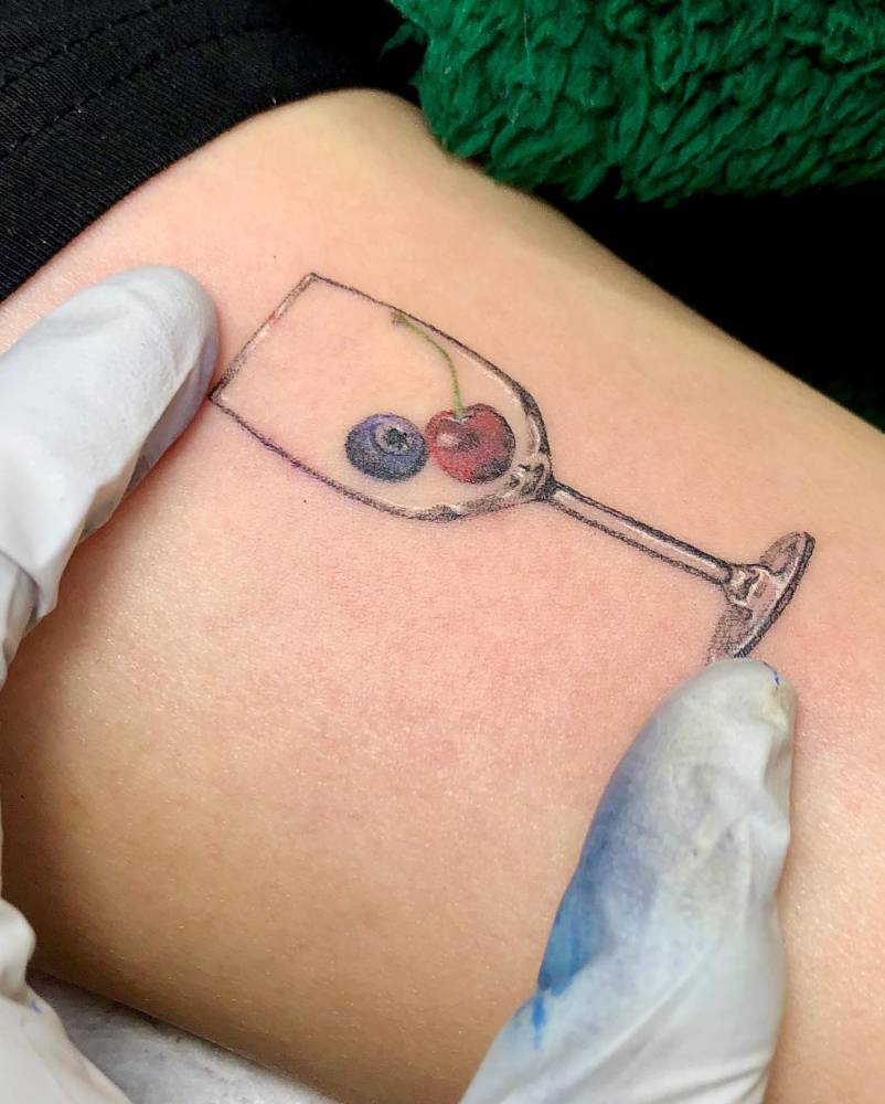 Wine glass, blueberry and cherry tattoo located on the bicep.