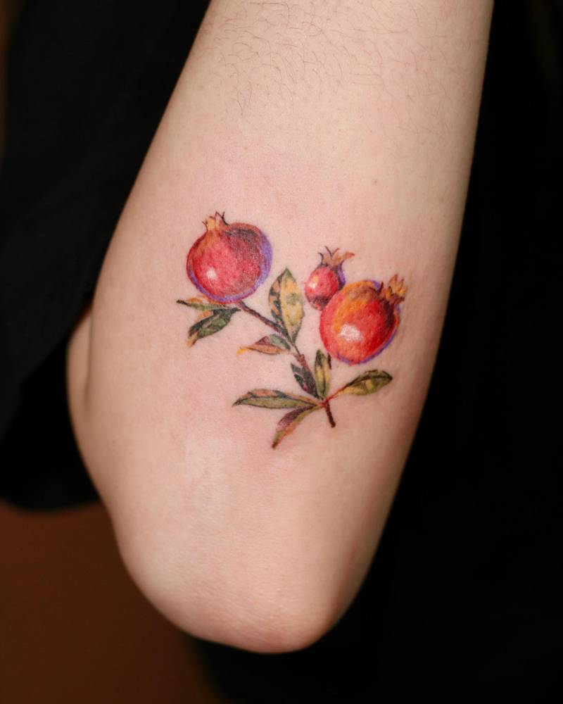Pomegranate tattoo located on the forearm, watercolor style.