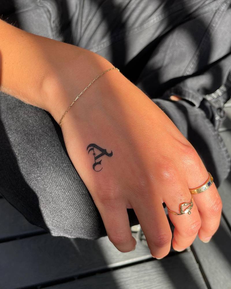 Hand poked letter "A" in gothic style tattooed on the hand.