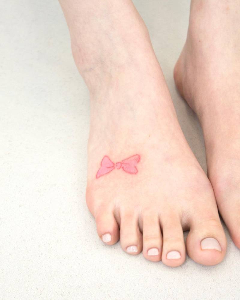Watercolor style ribbon bow tattoo located on the foot.