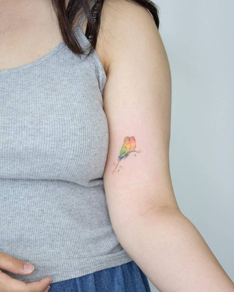 Lovebirds tattooed on the inner arm, watercolor style.