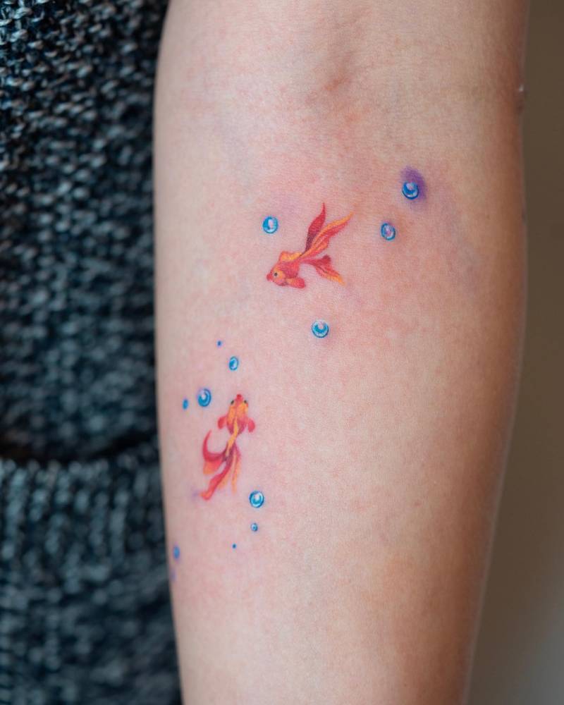 Watercolor style goldfish tattoo located on the inner forearm.