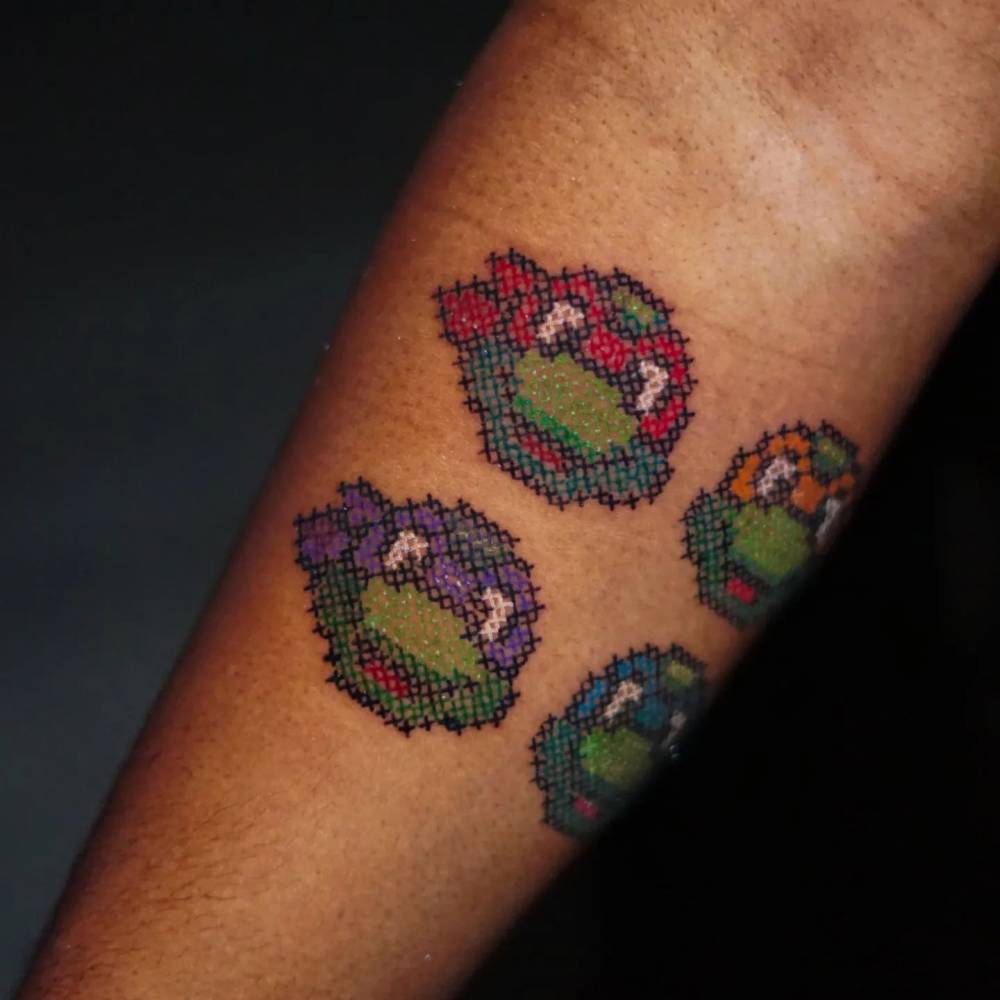 Teenage Mutant Ninja Turtles tattoo located on the inner forearm, cross stitch style.