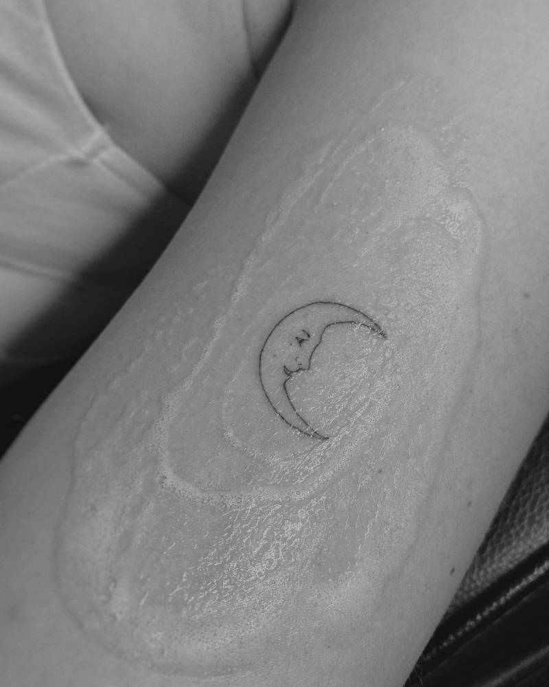 Minimalistic moon face tattoo done on the upper arm.