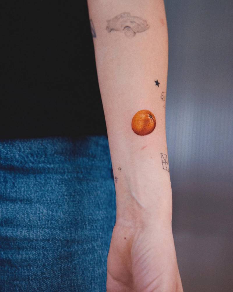 Micro-realistic orange tattoo located on the wrist.
