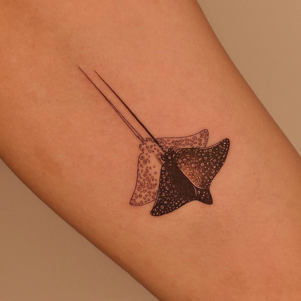 Illustrative style white-spotted eagle ray tattoo located on the inner arm.