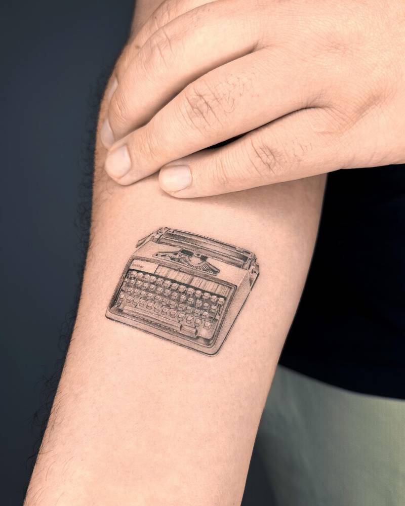 Micro-realistic typewriter tattoo placed on the inner forearm.
