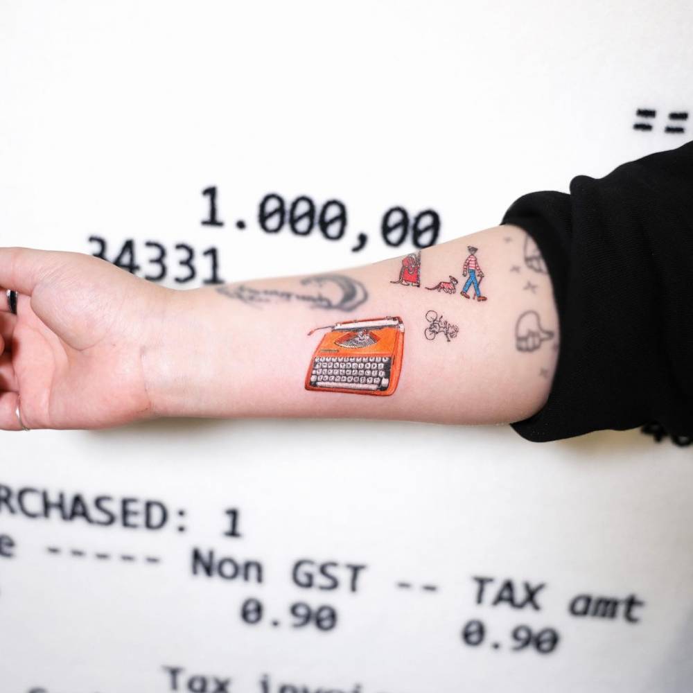 Micro-realistic style typewriter tattoo located on the inner forearm.