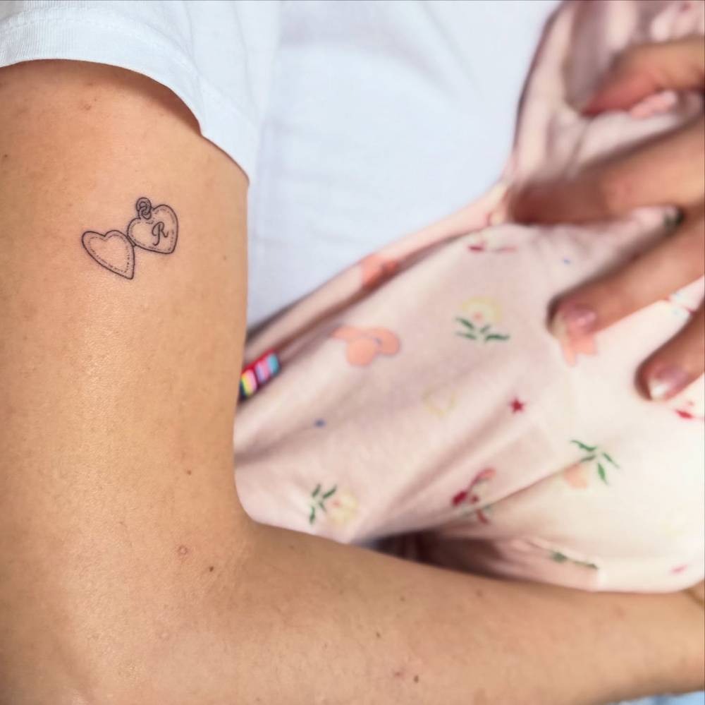 Hand poked heart pendant with the letter "R" tattoo located on the upper arm.